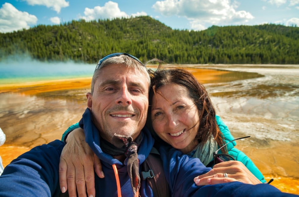 Happy couple making a selfie with the background of Grand Prismatic Spring Geyser, Yellowstone National Park.